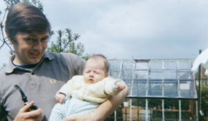Man holding baby in front of greenhouse