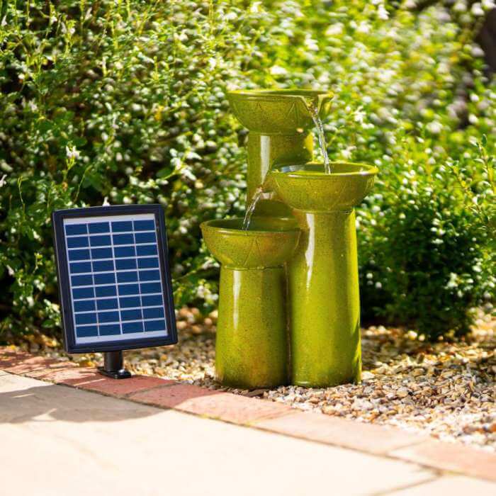 green vase bowl shaped solar water feature surrounded by greenery with solar panel next to it